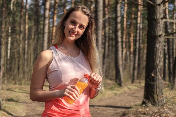 Sporty woman with orange smoothie at sunny day in the park — Stock Photo, Image