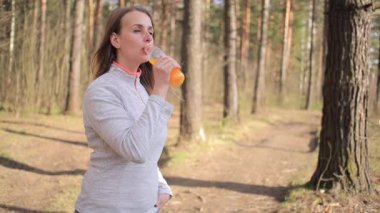 Parkta güneşli bir günde portakal suyu içen sportif bir kadın.