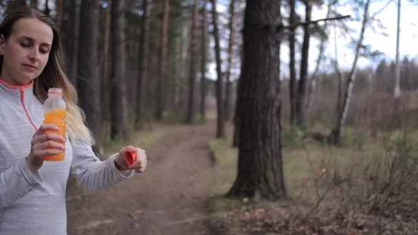 Спортивная женщина пьет апельсиновый смузи в солнечный день в парке — стоковое видео