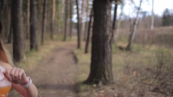 Sportieve vrouw drinkt sinaasappelsmoothie op zonnige dag in het park — Stockvideo