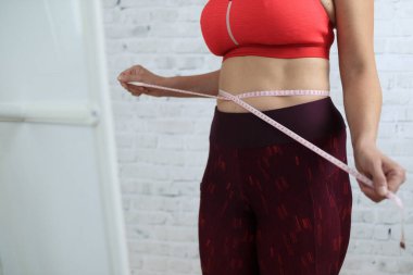 Genç bir kadın evinde aynanın yanında belini ölçmeye çalışıyor..