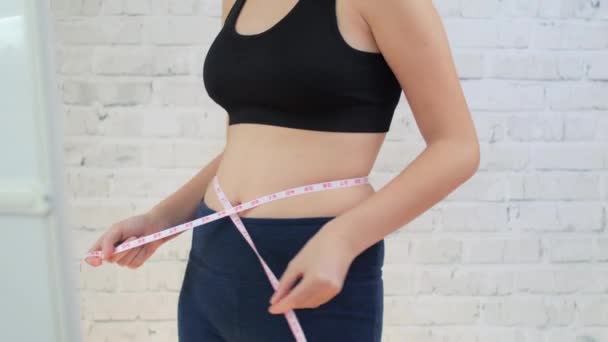Chica joven tratar de medir la cintura cerca del espejo — Vídeo de stock