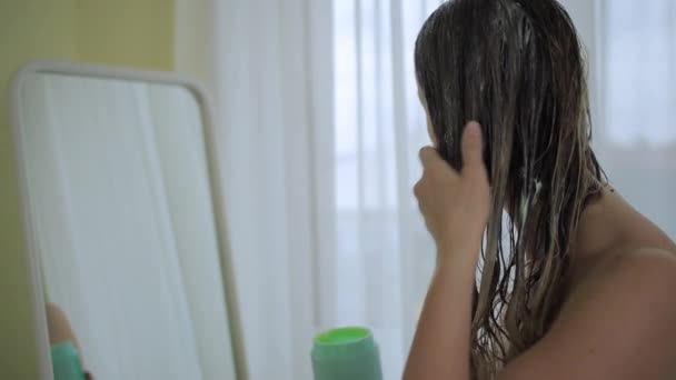 Vrouw in de buurt spiegel zet balsem of conditioner op het haar — Stockvideo