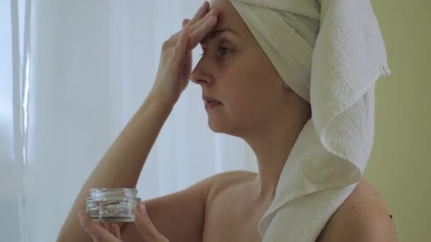 Женщина наносит крем для увлажнения на лицо после ванны — стоковое видео