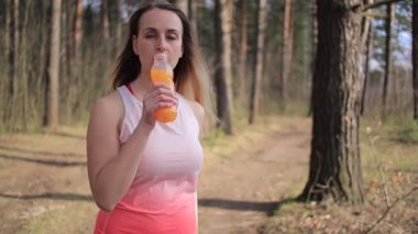 Parkta güneşli bir günde portakallı smoothie ile sportif bir kadın.