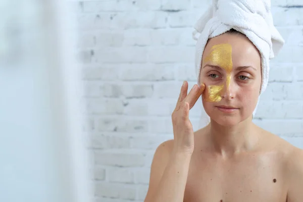 Vrouw die gouden hydrogel masker op gezicht aanbrengt — Stockfoto