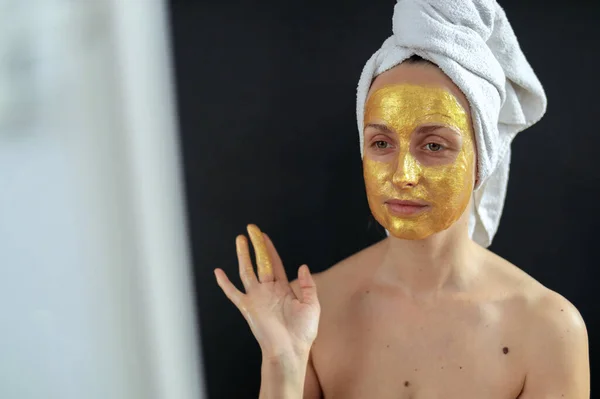 Женщина надевает на лицо золотую гидрогелевую маску — стоковое фото
