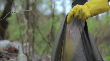 Ormanda plastik torba içinde cam şişeleri toplayan gönüllü bir kadın.