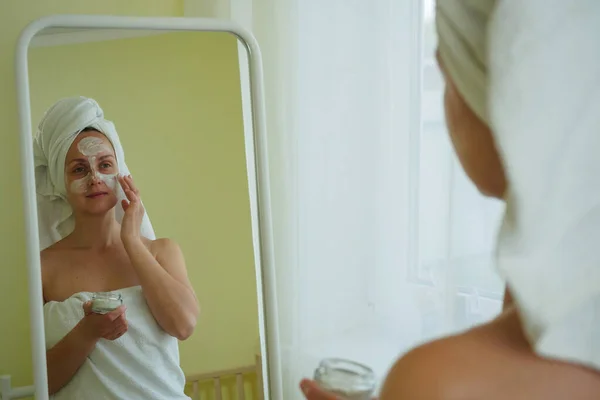 Женщина после ванной надевает маску на лицо — стоковое фото
