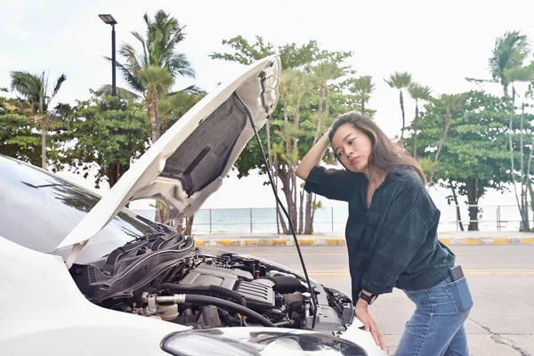 Stressed woman opening hood of broken car