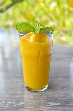 Sağlıklı mango smoothie frappe bir bardak üzerinde ahşap masa arka planda. 