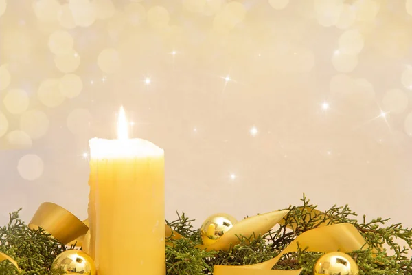 Рождественская копия пространства с зажженной жёлтой свечой, сосновыми ветвями, золотой атласной лентой и золотыми рождественскими шарами на светлом фоне — стоковое фото