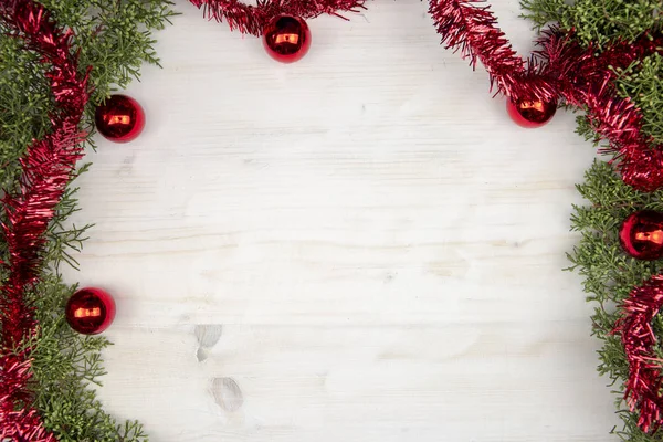 Świąteczna przestrzeń z gałązkami sosny, czerwoną girlandą i czerwonymi bombkami świątecznymi na jasnym drewnianym tle — Zdjęcie stockowe