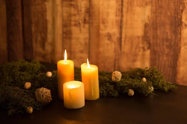 Минимальная рождественская концепция: три зажжённых свечи на тёмном деревянном столе и деревенская древесина окружающая с сосновыми ветвями и белыми естественными декорациями — стоковое фото