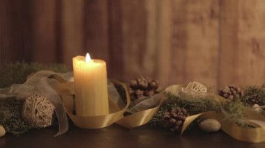 Hareketli mum alevleri, çam dalları, doğal çam kozalakları, altın saten ve beyaz organza süslemeleri olan bir Noel ortamını kapatın.