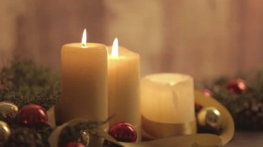 Hareketli mum alevleri, çam dalları, doğal çam kozalakları, kırmızı ve altın takılar, saten kurdele dekorasyonlarıyla bokeh etkisi altında çekilen bir Noel ortamını kapatın.