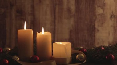 Hareketli alevler, çam dalları, doğal çam kozalakları, kırmızı ve altın takılar, bokeh etkisi altında çekilen saten kurdele süslemeleri ile Noel ayarı