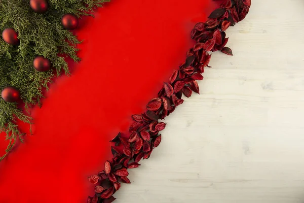 Flach liegender roter Weihnachtskopierraum mit diagonalem roten Streifen auf hellem Holzgrund, Tannenzweigen, roten Blütenblättern und roten Christbaumkugeln — Stockfoto