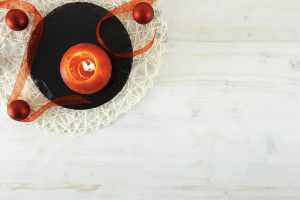 Flach liegender weihnachtlicher Kopierraum mit rotem Organza-Band, roter brennender Kerze, schwarzem runden Kalksteinteller auf hellem Holzhintergrund — Stockfoto