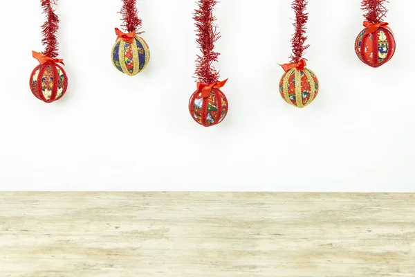 Weihnachtskopierraum: fünf handgefertigte Christbaumkugeln in der Decoupage-Technik, die von oben mit einem rot glänzenden Kranz auf weißem Hintergrund und einem hellen Holzsockel unten aufgehängt wurden — Stockfoto