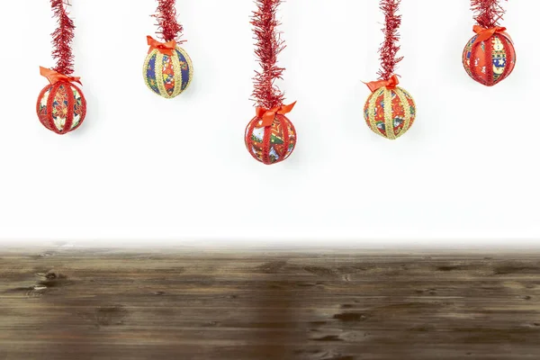 Weihnachtskopierraum: fünf handgefertigte Christbaumkugeln in Decoupage-Technik, die von oben mit roter glänzender Girlande auf weißem Hintergrund und dunklem Holzsockel unten aufgehängt wurden — Stockfoto