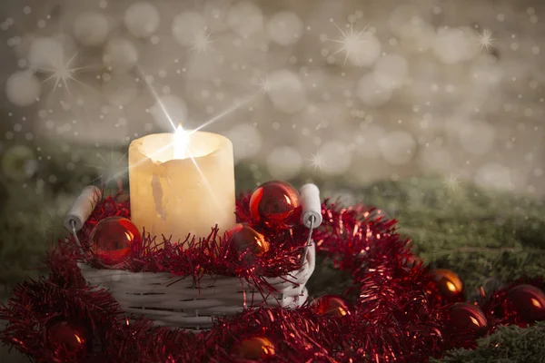 Рождественская концепция: зажженная свеча с эффектом крестовых звёзд в белой потрепанной корзине с красными рождественскими безделушками, красным декоративным венком, натуральной сосновой веткой, деревянным фоном и снежным эффектом — стоковое фото