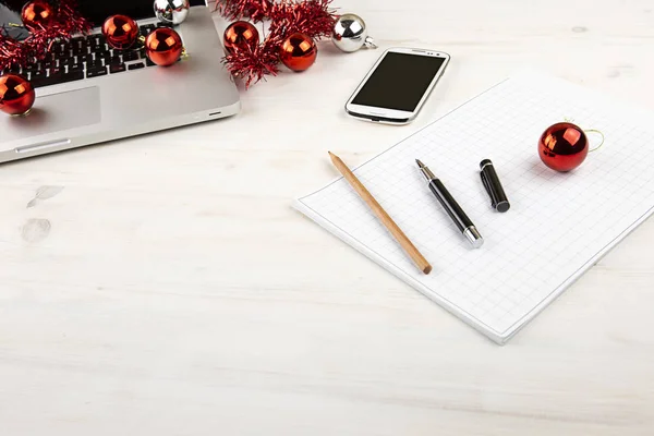 Számítógépes munka a karácsonyi ünnepek koncepció: könnyű fa asztal nyitott alumínium laptop, piros dekoráció, piros baubles, okostelefon, blokk jegyzetek, ceruza és toll blokk jegyzet — Stock Fotó