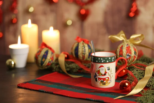 Χριστουγεννιάτικη κούπα με άδεια ετικέτα τσαγιού σε Χριστουγεννιάτικο τραπεζομάντηλο με γύρω κλαδιά πεύκου, στολίδια με αναμμένα κεριά και χριστουγεννιάτικη διακόσμηση σε ξύλινο φόντο με bokeh αποτέλεσμα — Φωτογραφία Αρχείου