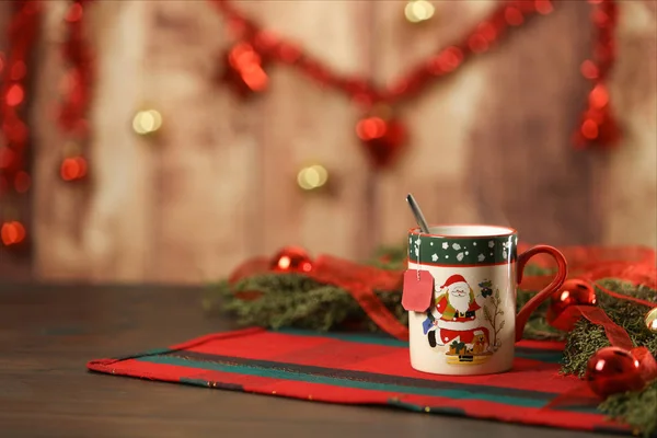 Noel arkaplanına boş çay etiketi asılmış çam dalları, kırmızı takılar ve bokeh efektli ahşap arka planda asılı Noel süsü.
