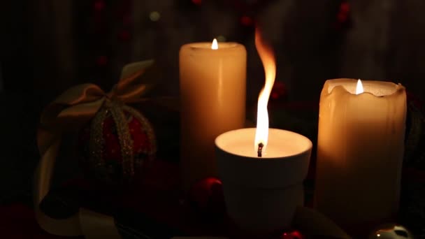 クリスマスムード 3つのキャンドル 前景に大きな炎を持つ1つ 赤と金色のボール デカッページボール サテンゴールドリボン 低光とボケ効果で撮影されたクリスマスの装飾 — ストック動画