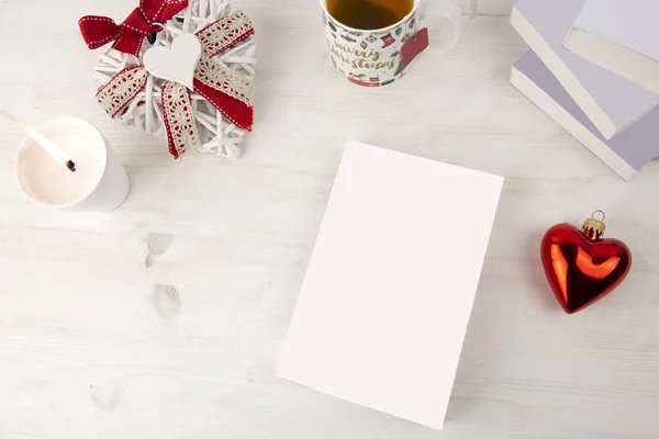 Karácsonyi kilátás felülről egy könyv bemutató: könyv üres borító fehér gyertyákkal, karácsonyi díszített csésze tea, piros szív csecsebecse, egy kopott díszített fehér szív könnyű fa asztalon — Stock Fotó