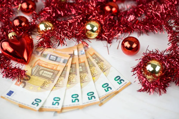 Noel parası iş konsepti: kırmızı ve altın takılar ve hafif ahşap masa üzerindeki çelenk dekorasyonlu yaklaşık 50 avroluk banknotlar