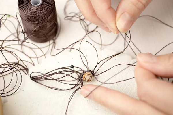 Lifestyle concept, reinvent your life and your job: close-up detail of woman hands making macrame knotted jewel with the fingers that tie the nylon thread around the diaspro natural stone — Stock Photo, Image