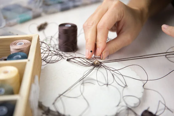 Lifestyle concept, work from home to reinvent your life: close-up detail of woman hands making macrame knotted jewel with some colored thread spools in foreground and bokeh effect — Stock Photo, Image