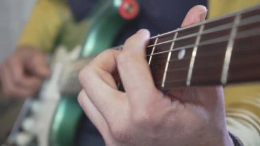 Metalik yeşil bir elektro gitarda akor, sololar ve sololar çalan bir gitar ustasının boynunda kayan elinin yakın çekimi.