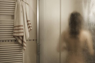 Seksi çıplak esmer kadın banyo kabininde duş alıyor. Modern tasarım banyosunda sisli camdan görülüyor.