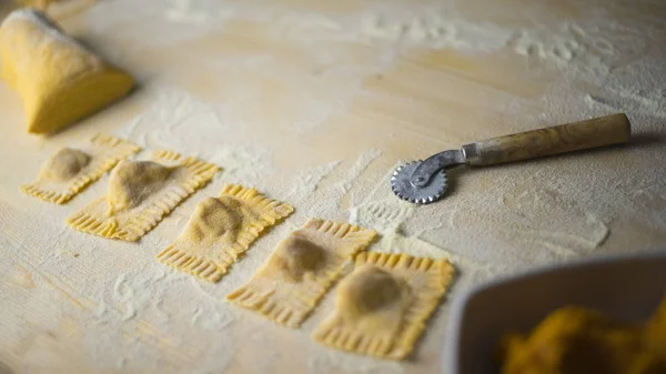 Closeup de abóbora ravioli vegan, massas tradicionais italianas, massas caseiras acabado de fazer, com a massa de farinha de trigo duro, a roda de corte e farinha de trigo espalhados sobre a mesa de madeira leve — Fotografia de Stock