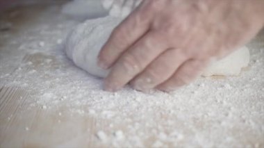 Evdeki pizza hamurunu beyaz unlu açık ahşap bir masada yoğuran adamların yakın çekimi.