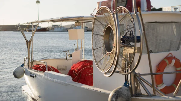 A moored fishing boat is waiting to set sail water while the sun reflects on the sea early in the morning with the winch of the fishing net in the foreground — Stock Photo, Image