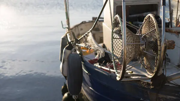 Швартованная рыбацкая лодка ждет, чтобы установить парусную воду, в то время как солнце размышляет о море рано утром с лебедкой рыболовной сети на переднем плане — стоковое фото