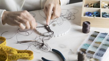 Yaşam tarzı konsepti, hayatınızı yeniden keşfetmek için evden çalışmak: kadın ellerine yakın plan taş boncuklar ve açık ahşap masa üzerinde aletler ile makrome düğümlenmiş mücevherler yapmak