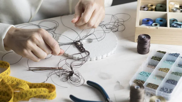 Lifestyle concept, work from home to reinvent your life: close-up of woman hands making macrame knotted jewelry with stone beads and tools on light wooden table — Stock Photo, Image