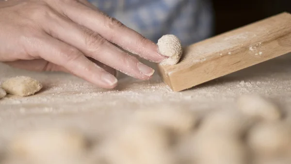 Close up process of homemade vegan gnocchi pasta with wholemeal flour making. The home cook crawls on the special wooden tool the gnocco , traditional Italian pasta, woman cooks food in the kitchen