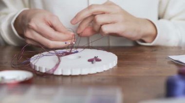 Yaşam tarzı konsepti, hayatınızı yeniden keşfetmek için evden çalışmak: Makrome düğümleri yapan kadın ellerinin yakın çekimi fuşya ipliği, ahşap masadaki kumihimo aletlerinde bir küpe yaratmak