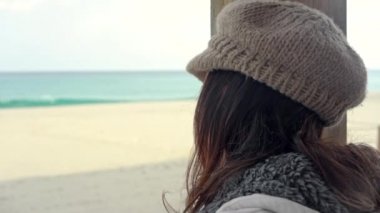 Kışın fırtınalı bir gökyüzü ile deniz kenarındaki kapalı bir barın güneş odasındaki tahta direğe yaslanmış genç bir kadın dalgın ufka bakar.