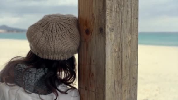冬日里 在海边一个紧闭的酒吧的日光浴室里 一个年轻的女人靠着一根木棍 头顶着暴风雨的天空 凝视着沉思的地平线 — 图库视频影像