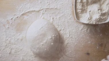 Yavaş çekimde pizza hamuruna un serpiştiren ve evde beyaz un ile bırakılması için masaj yapan bir adamın elleri görülüyor.
