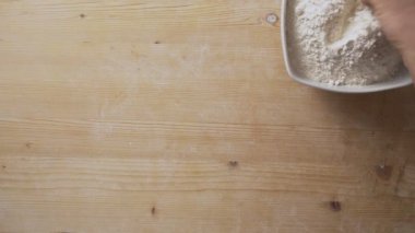 Üst görüntü, pizzayı elle yoğurmaya hazır hale getirmek için tahtaya un serpiştiren bir adamın elleri yavaş çekimde.
