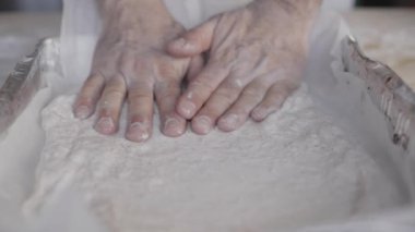 Coronavirus kilitleme konsepti için evde kal: evde pizza yap. Yavaşça yaklaşan adam, elleri hafif ahşap bir çalışma masasında bir yemek tepsisinin içinde pizza hamurunu yuvarlıyor.