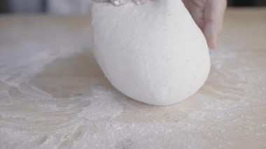 Coronavirus kilitleme konsepti için evde kalın: evde ekmek ve pizza yapın. Hafif ahşap bir çalışma masasında hamuru yoğuran bir adamı yavaş çekimde yakından çek. Ev yapımı ekmek ve pizza.